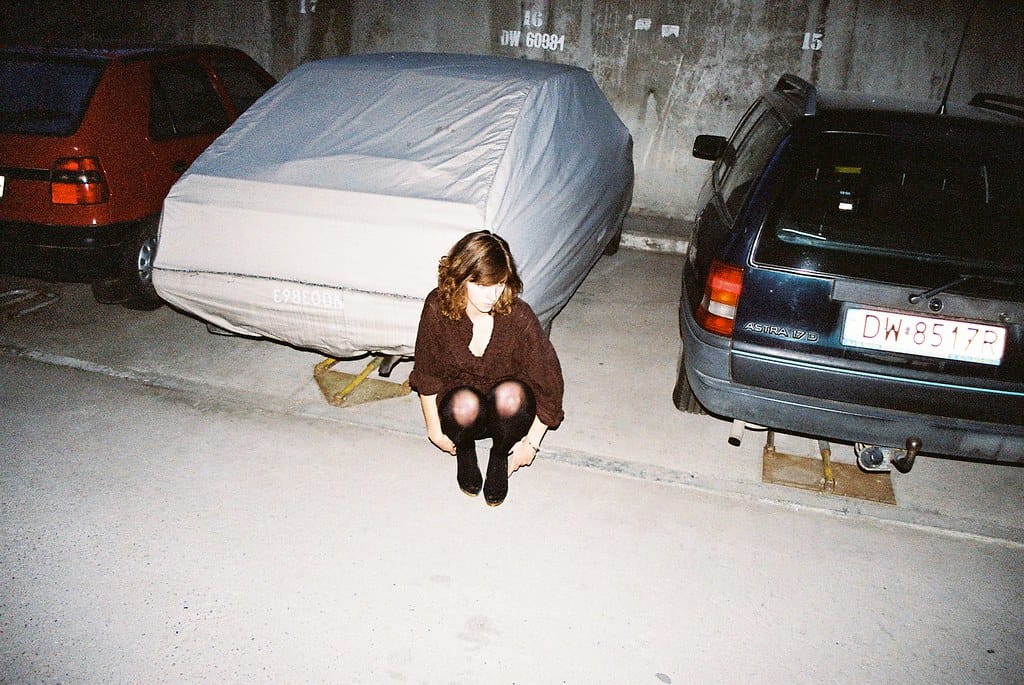 Young woman squatting on the ground in a parking garage with cars around her.