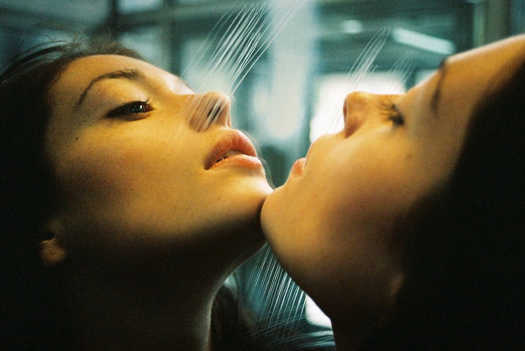 A young woman rests her chin on a mirror, reflecting her own image.
