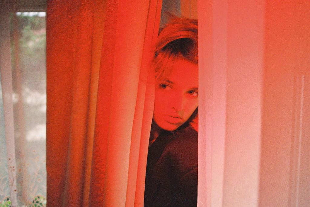 Young woman peeking through red curtains, her face partially obscured by the fabric.