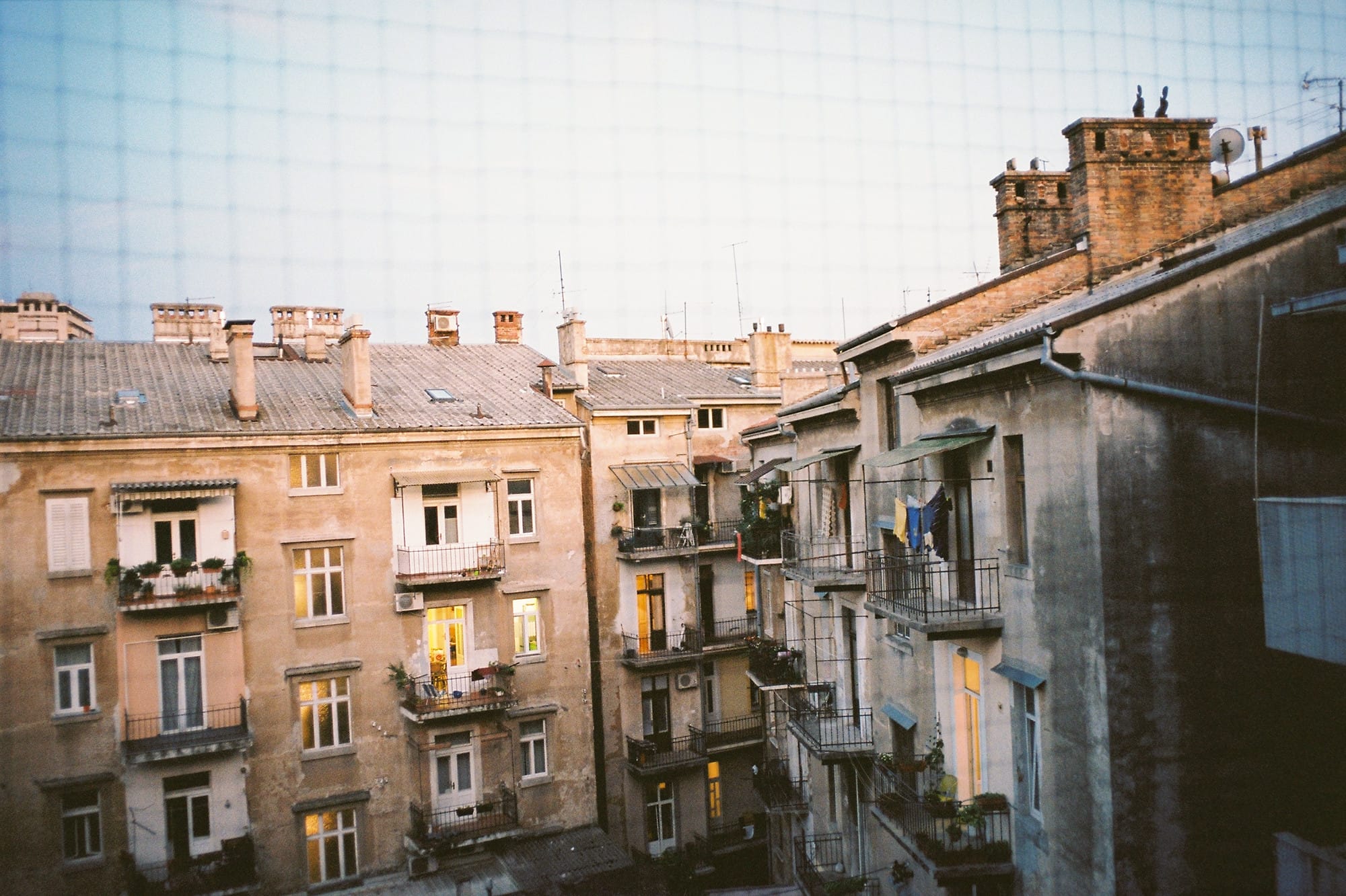 A view of an old, weathered building and its balconies and chimneys, captured from next door.