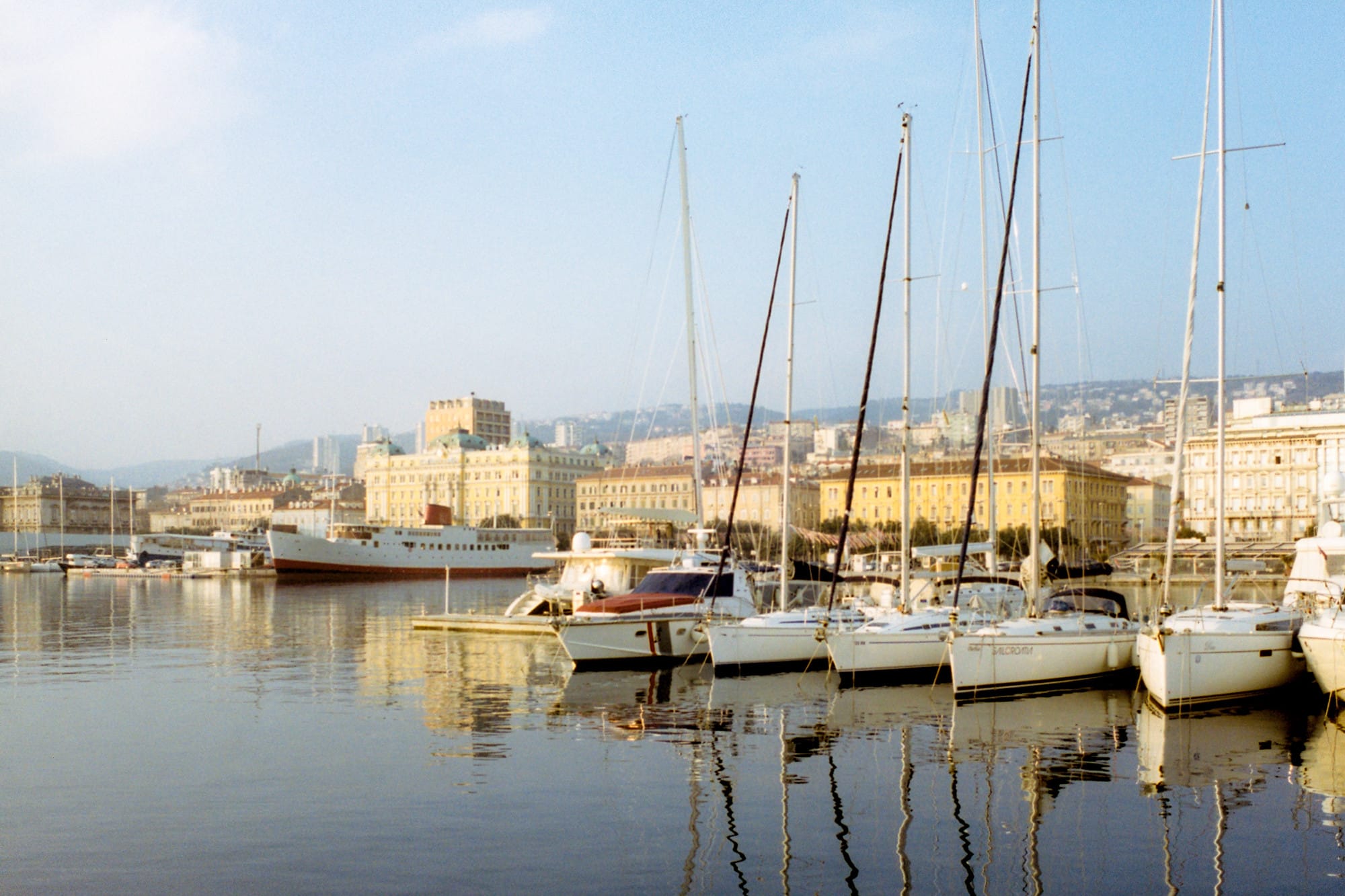 Sailboats and yachts docked in a harbor in Rijeka, with historic buildings in the background.
