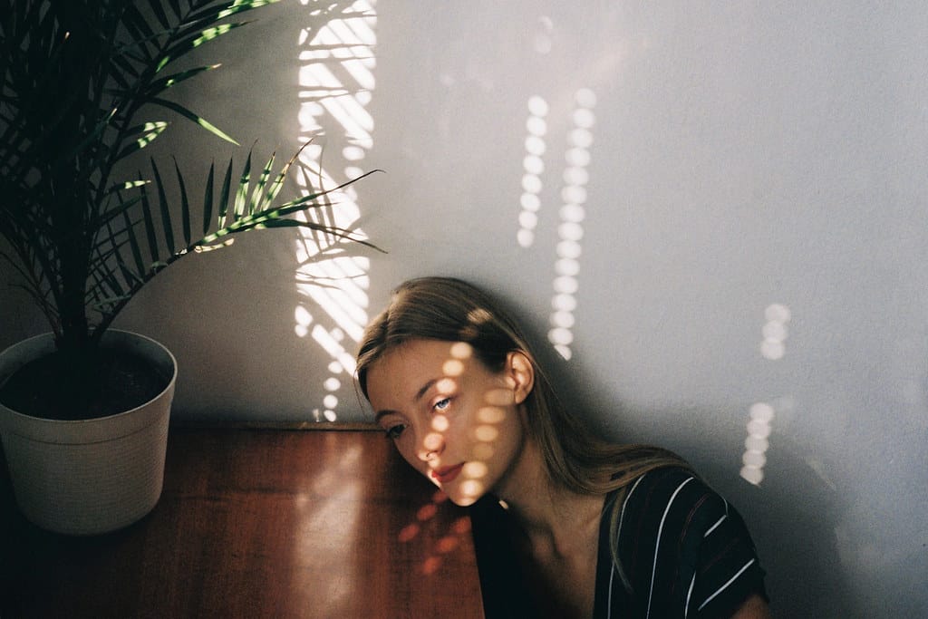 Young woman resting her head on an end table, her face lightly sun-kissed.