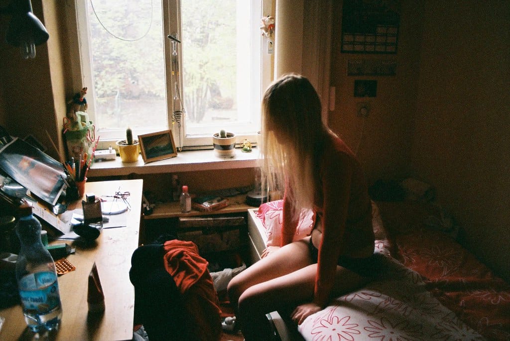 Window-lit young woman sitting on a bed in her cozy bedroom.