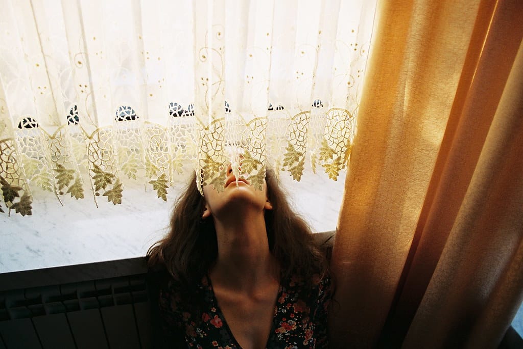 Young woman resting her head on a window sill, bathed in warm light.