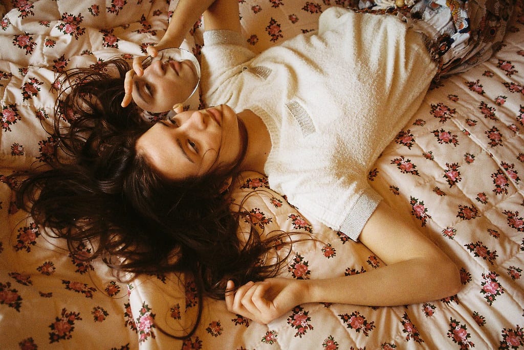 Young woman lying in bed, holding a mirror that reflects her face.