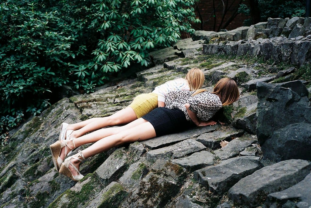 Two girls lying on a stones, each wearing a dress and jacket.