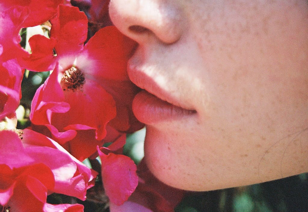 A freckle-faced girl takes in the scent of vibrant red blossoms.