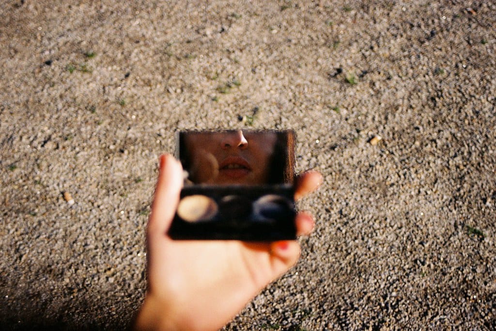 Hand holding an open makeup compact with a reflection of a young woman's face.