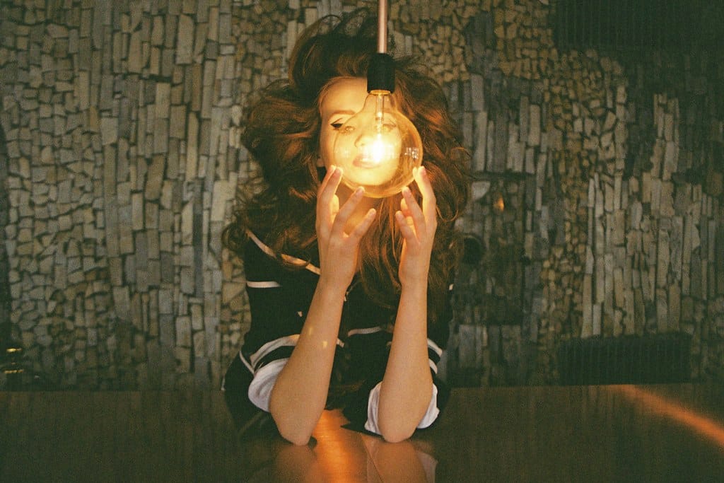 Woman holding a lit lightbulb close to her face in a dark room.