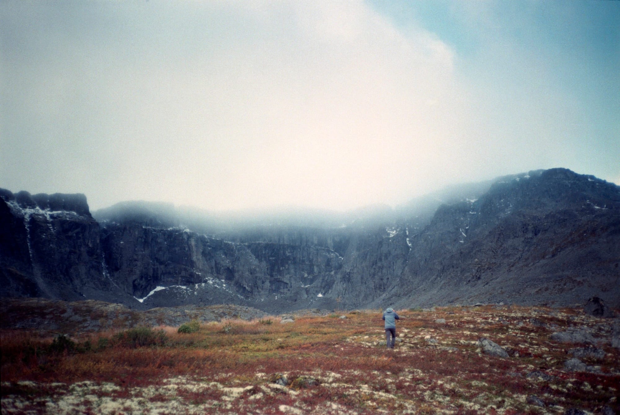 Serene, rugged landscape featuring a lone individual on a rocky terrain, overlooking a misty valley surrounded by high cliffs under a clear sky.