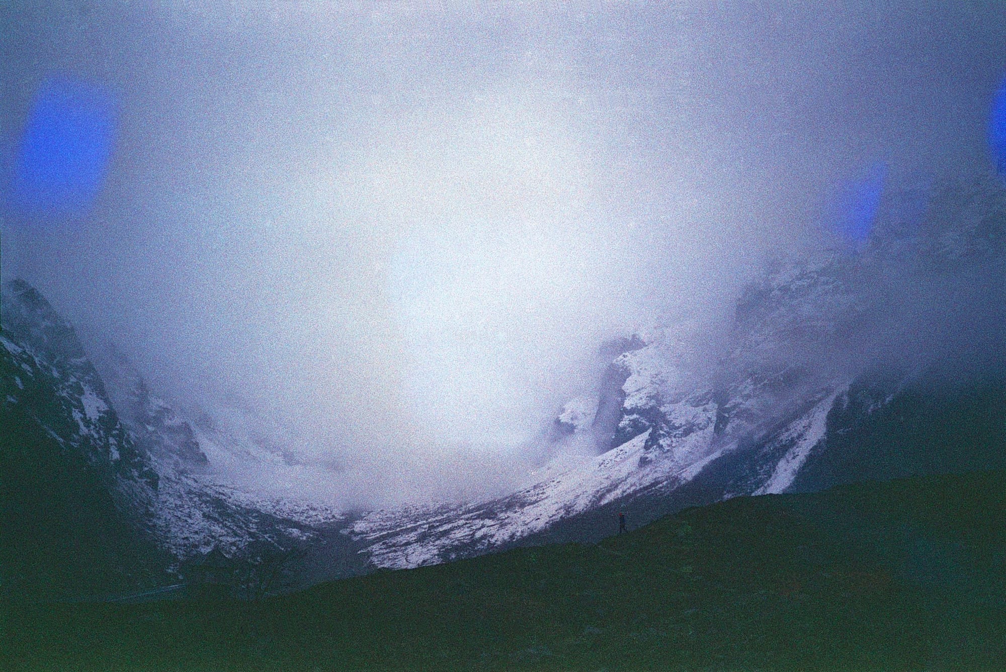 Serene, foggy mountain scene with snow-capped peaks and a lone figure walking down a hill in the foreground.