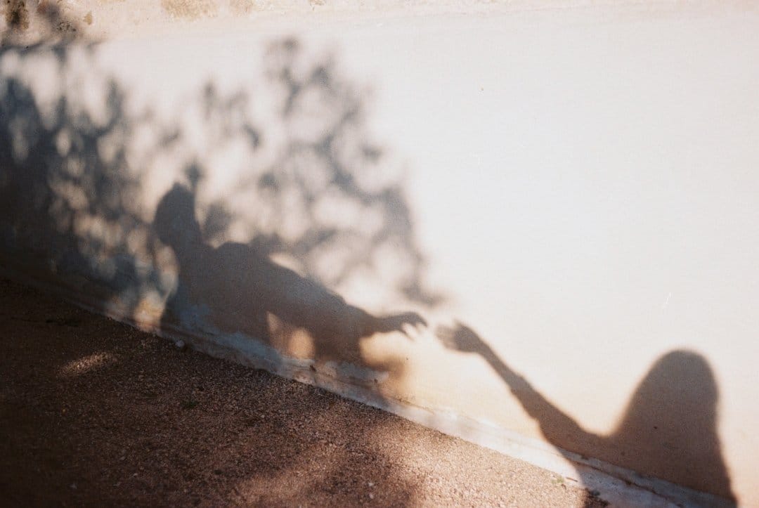 Silhouette of a man and woman on a wall and sidewalk, with the man extending his hand to hers.