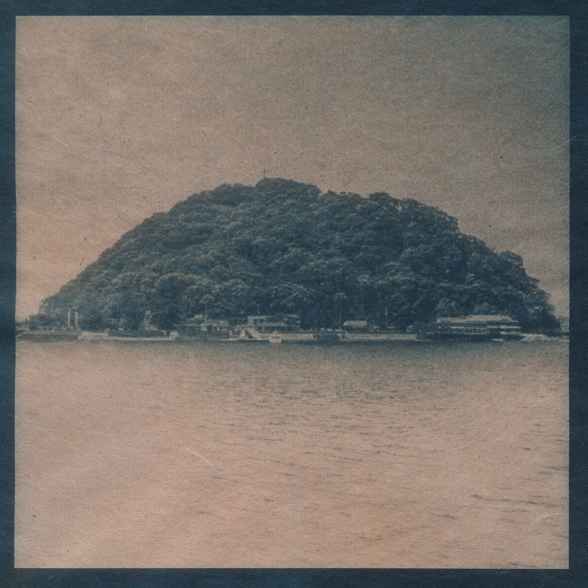 A cyanotype photograph of a small, forested island situated in calm waters, with buildings visible along the shoreline.