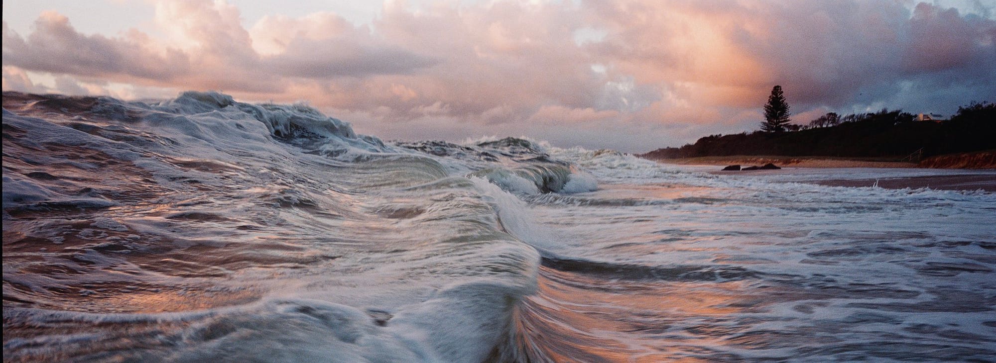 Stunning seascape at daybreak featuring turbulent waves and a sky illuminated by the sunrise's glow.