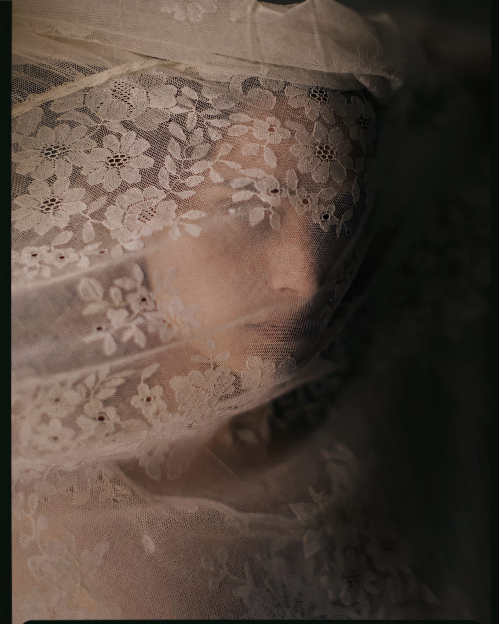 Young woman with lace covering her face and upper body, featuring intricate floral patterns.