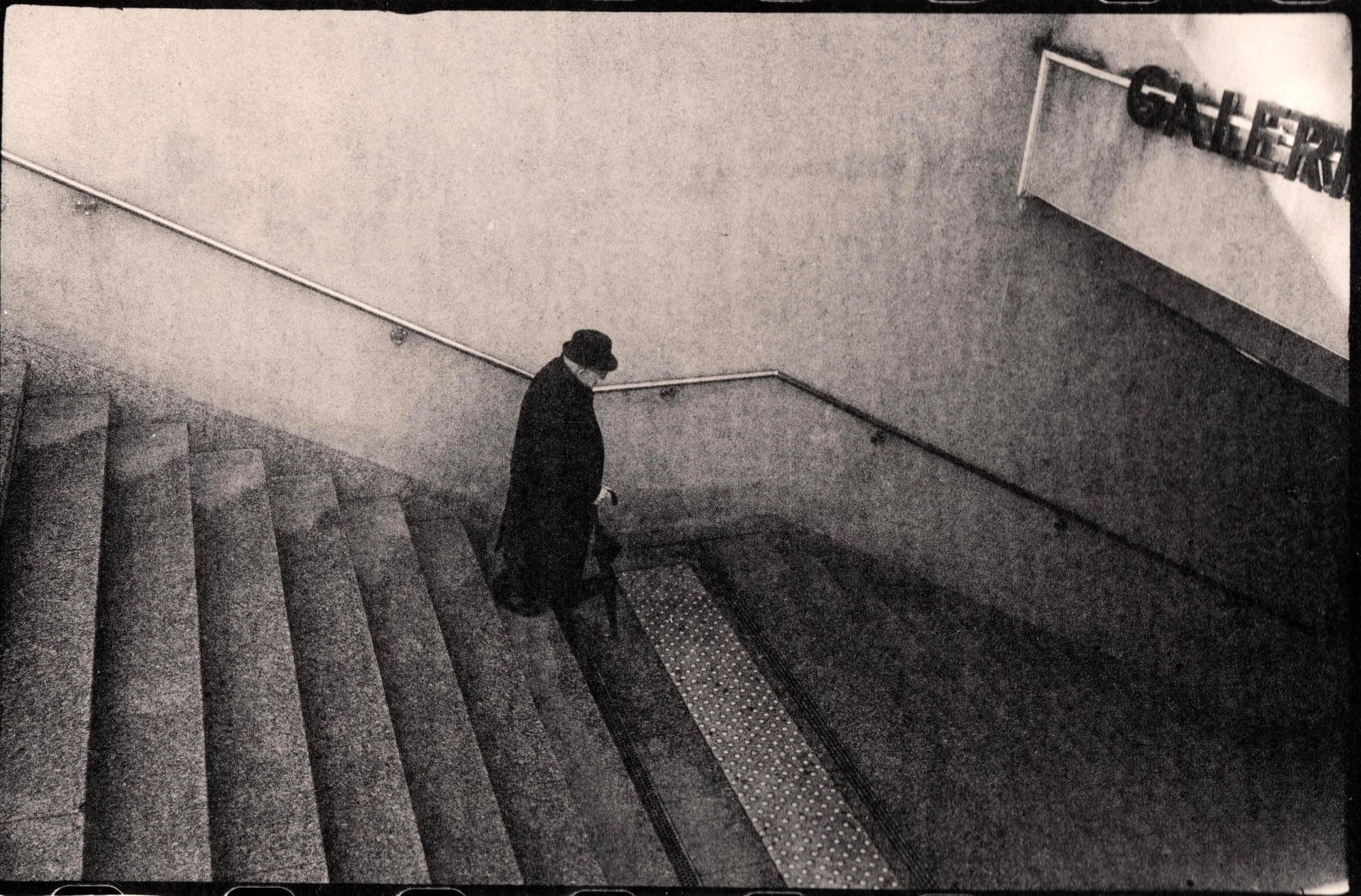 A lone figure descending stairs in a subway, wearing a long coat.