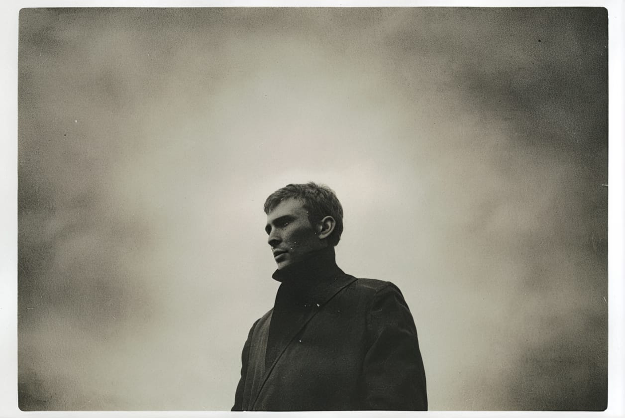 A black and white portrait of a man in a dark coat looking off into the distance.