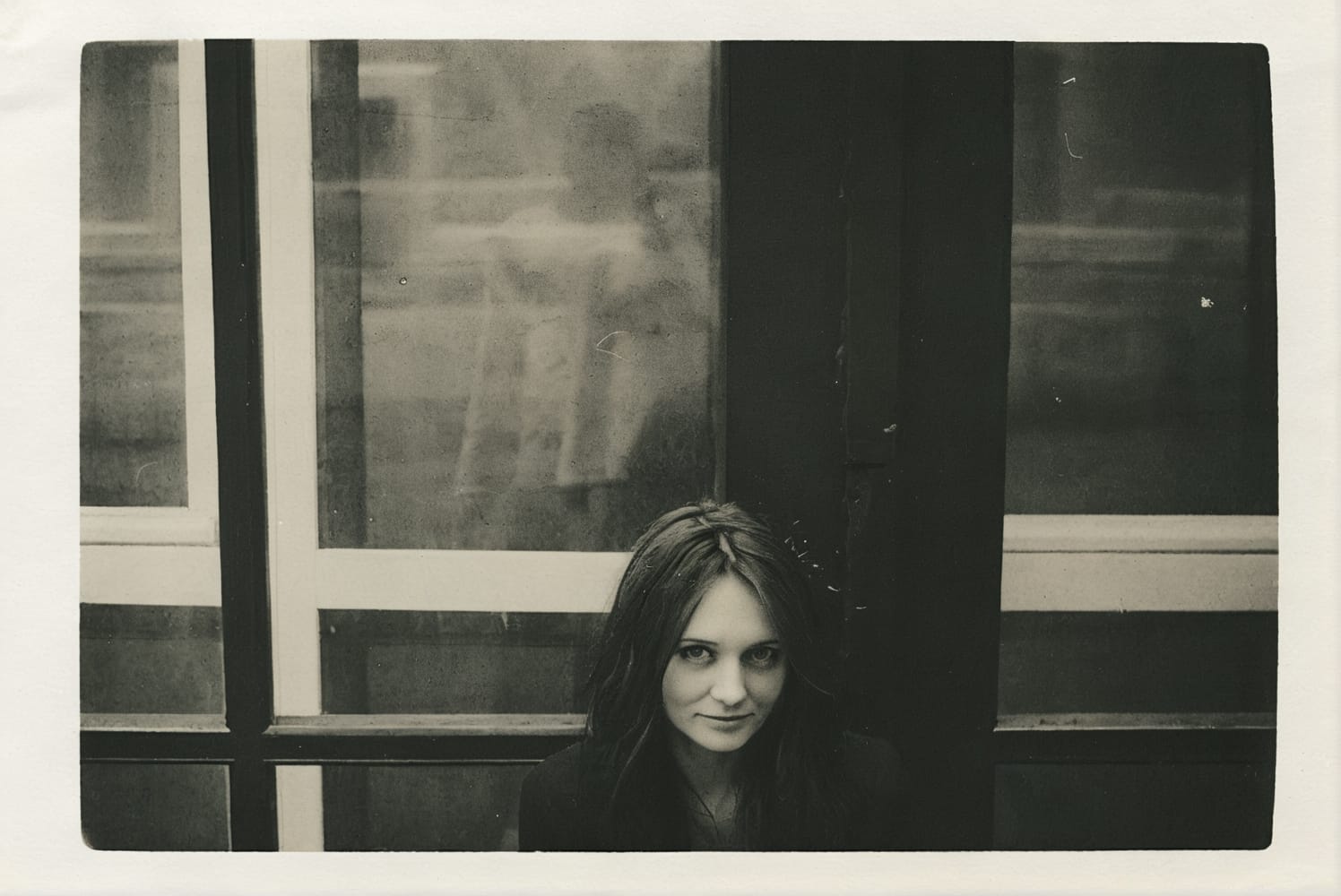 Retro portrait of a woman with long dark hair, sitting in front of a window.