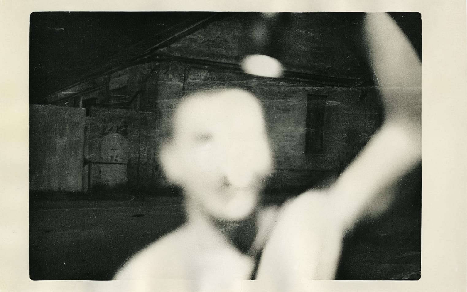 Monochrome photo of a person with a blurred visage, captured in front of a building.