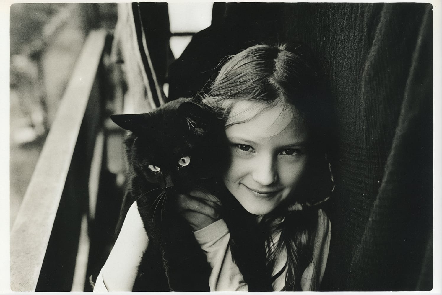 A black and white photograph of a young girl holding a black cat.