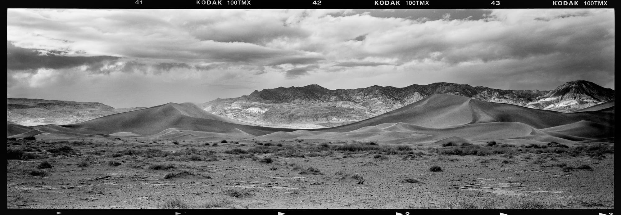Black and white landscape of rolling desert hills with distant mountains under a cloudy sky.