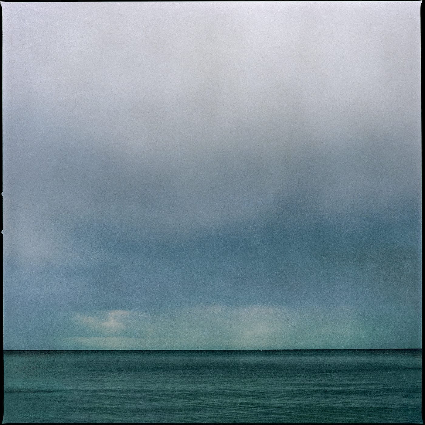 Tranquil seascape featuring a defined horizon line, gentle waves and a cloudy sky with varying shades of blue.