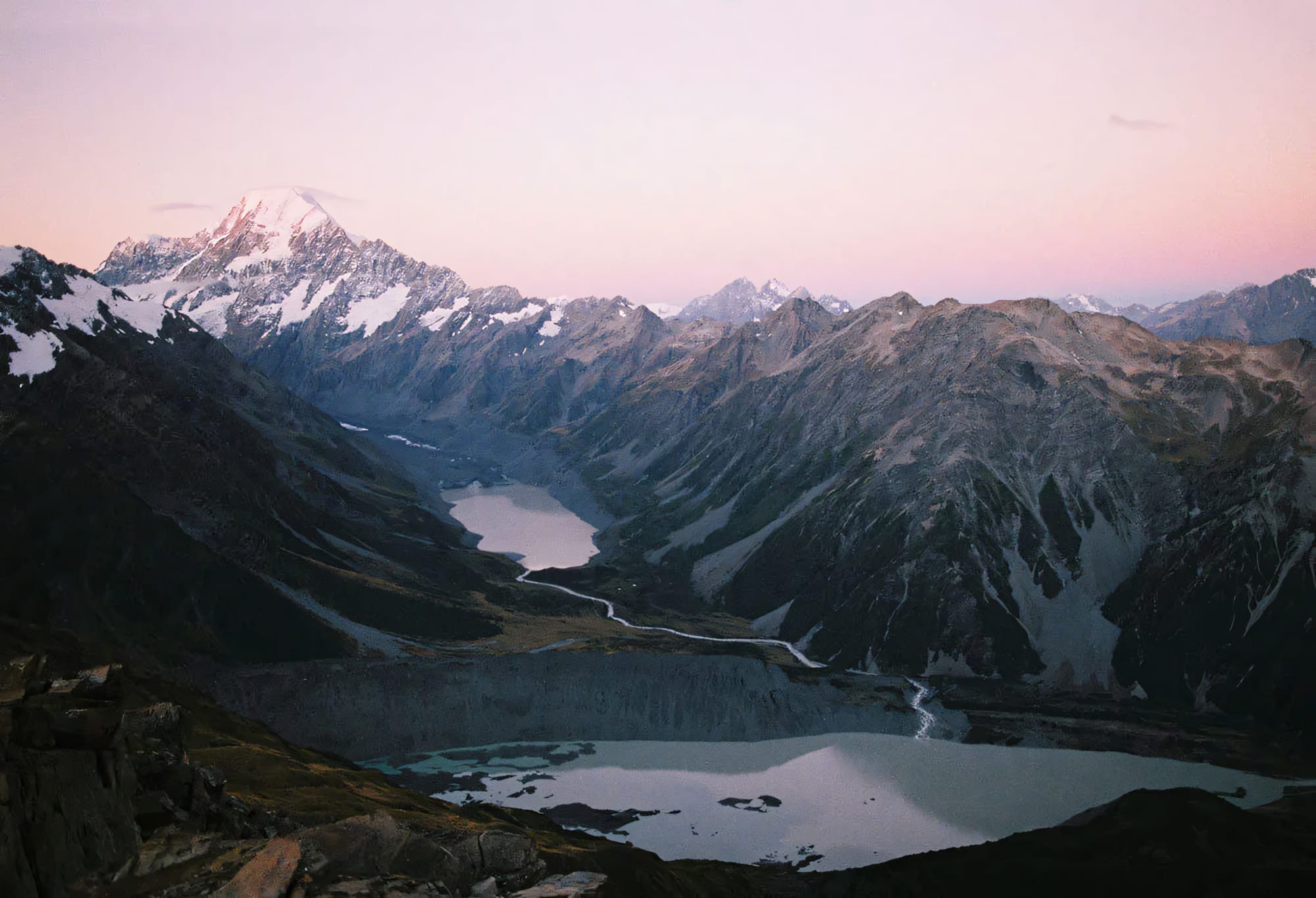 Mountain range with snow-capped peaks at dusk, reflecting in a serene alpine lake.