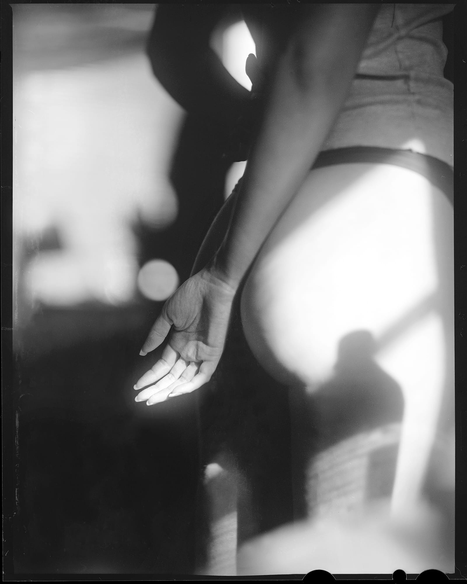 A black and white photo of a woman's bottom with her arm extended downward, palm open.