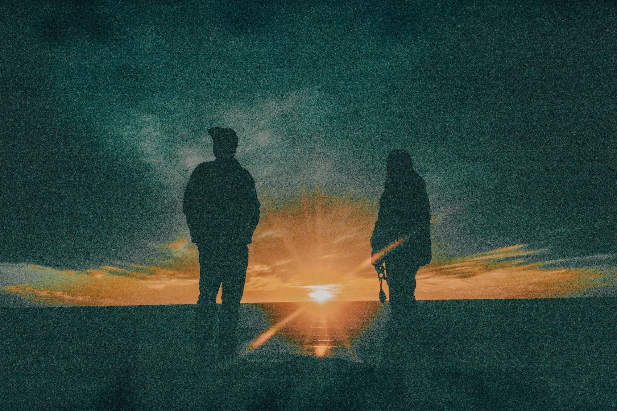Silhouette of two people watching a sunset over a body of water.
