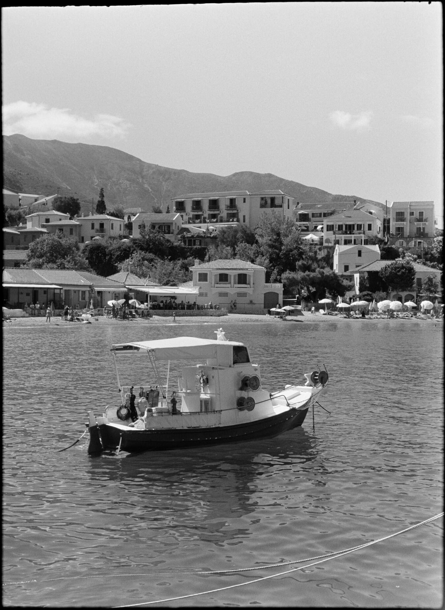 A small boat anchored in a calm bay with a coastal village in the background.
