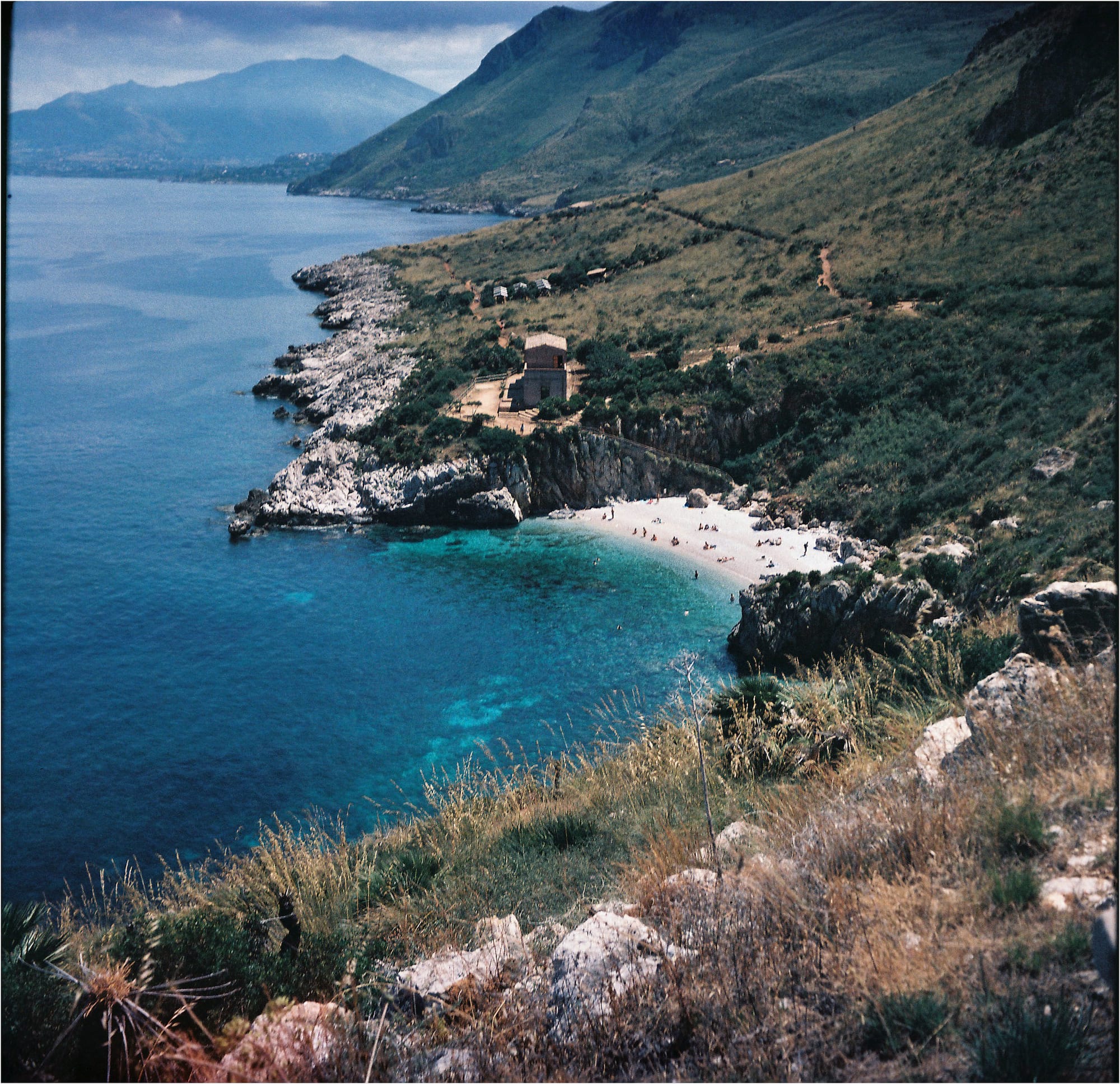 A secluded beach with clear turquoise waters, rugged cliffs, and lush greenery.