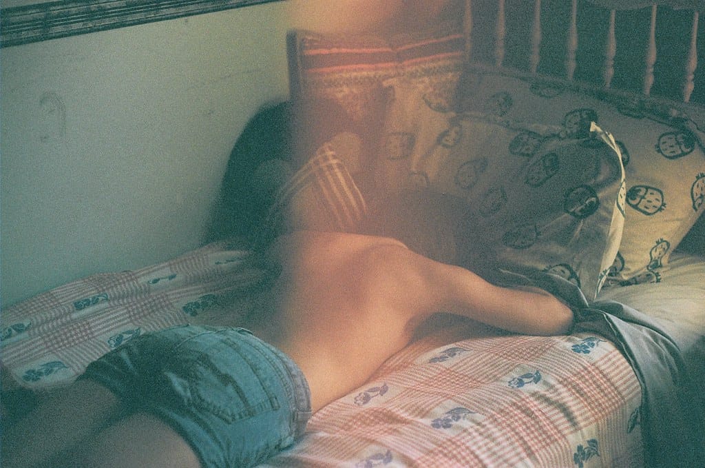 Brunette lying on a bed with patterned sheets, partially obscured by a light leak.