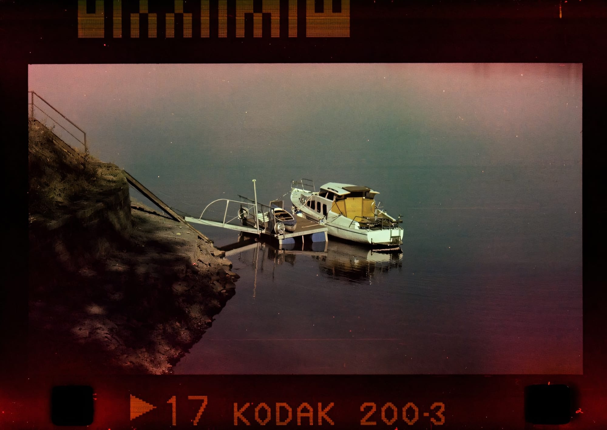 Boat docked at a small pier with a rocky shoreline and calm water.