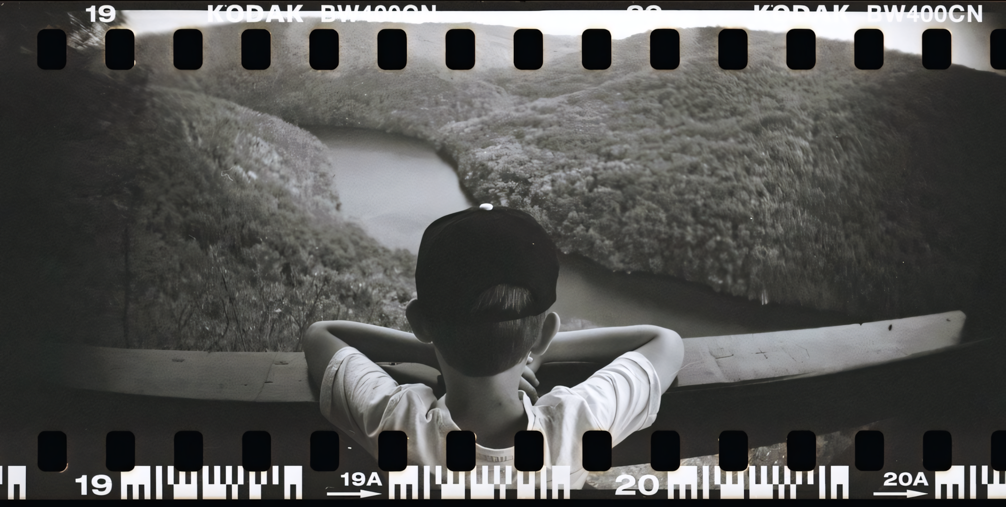 Kid standing on a high bridge looking down at a river in a valley.