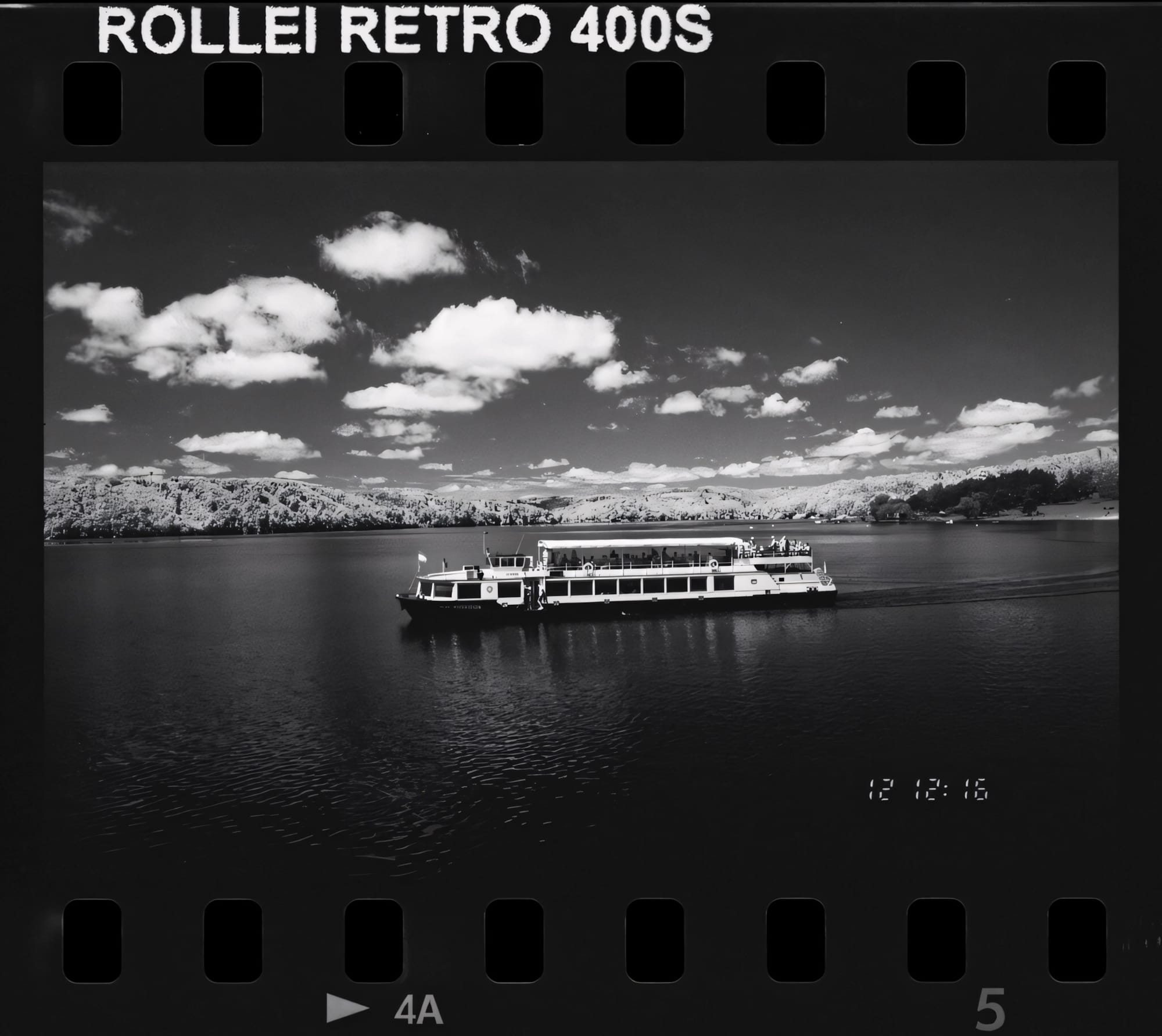 Black and white photo of a boat on a tranquil lake with hills in the background.