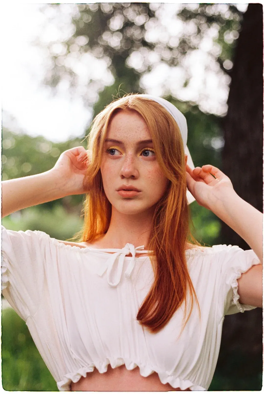 Model in white vintage outfit standing in sunny park on Kodak Vision3.