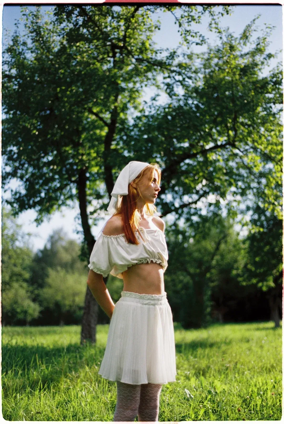 Red-haired model in white off-shoulder top with bokeh background on film.