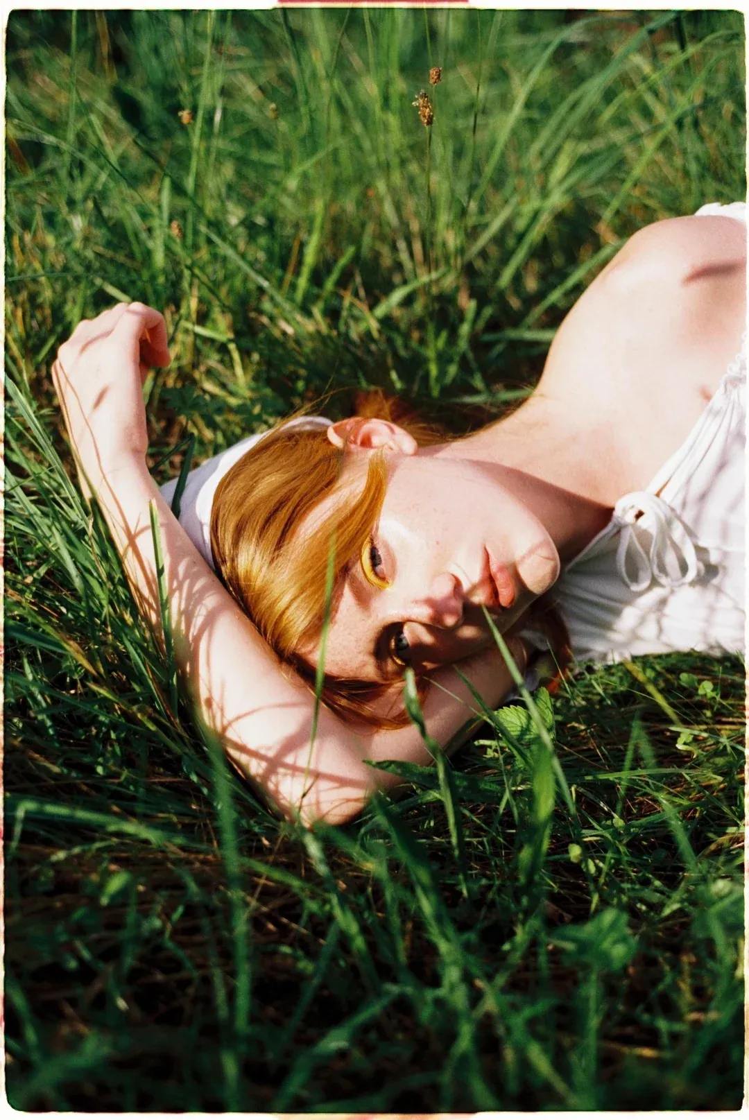 Red-haired model lying in grass looking up shot on cinema film stock.