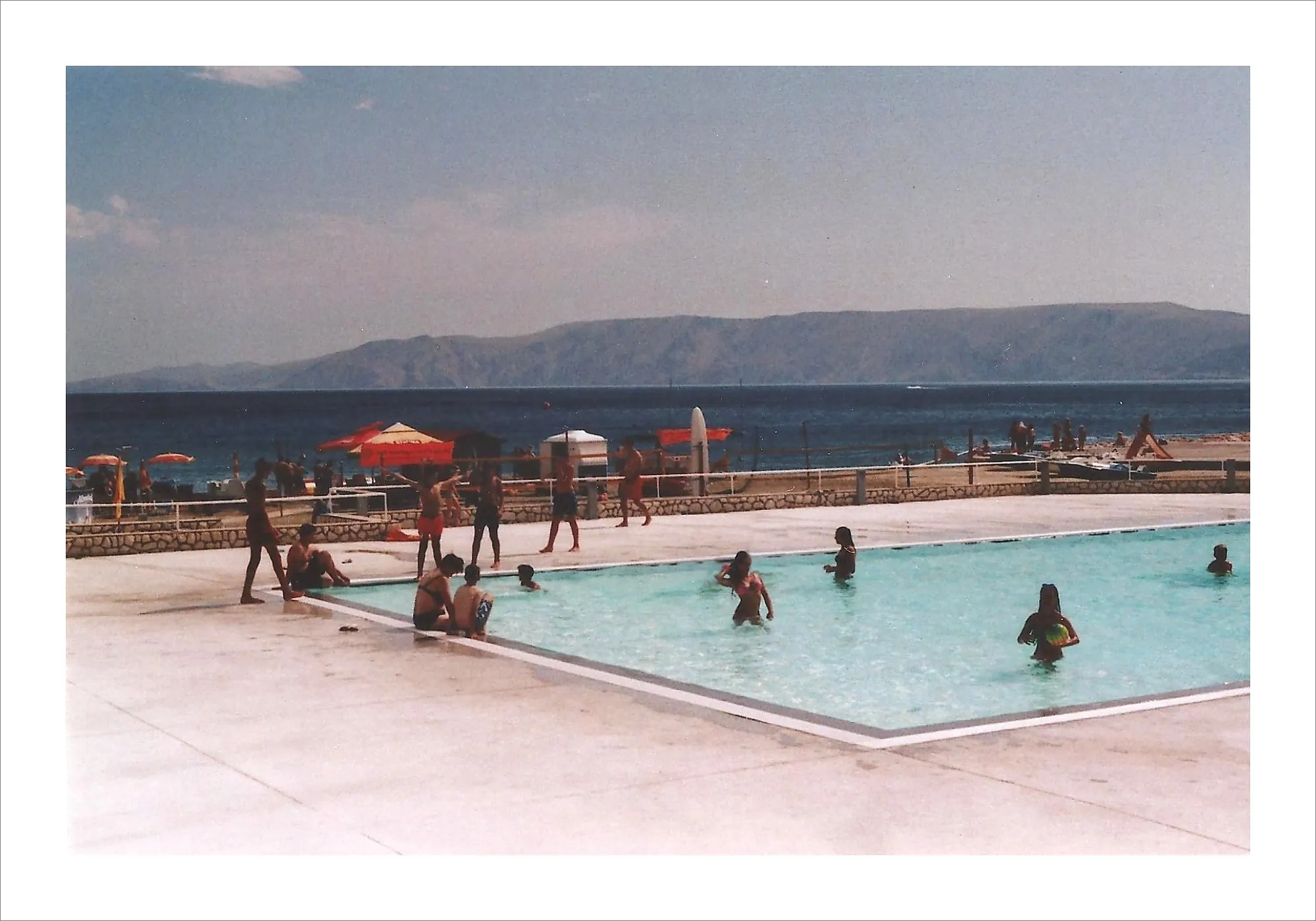 People swimming in Adriatic coastal pool with mountains beyond.
