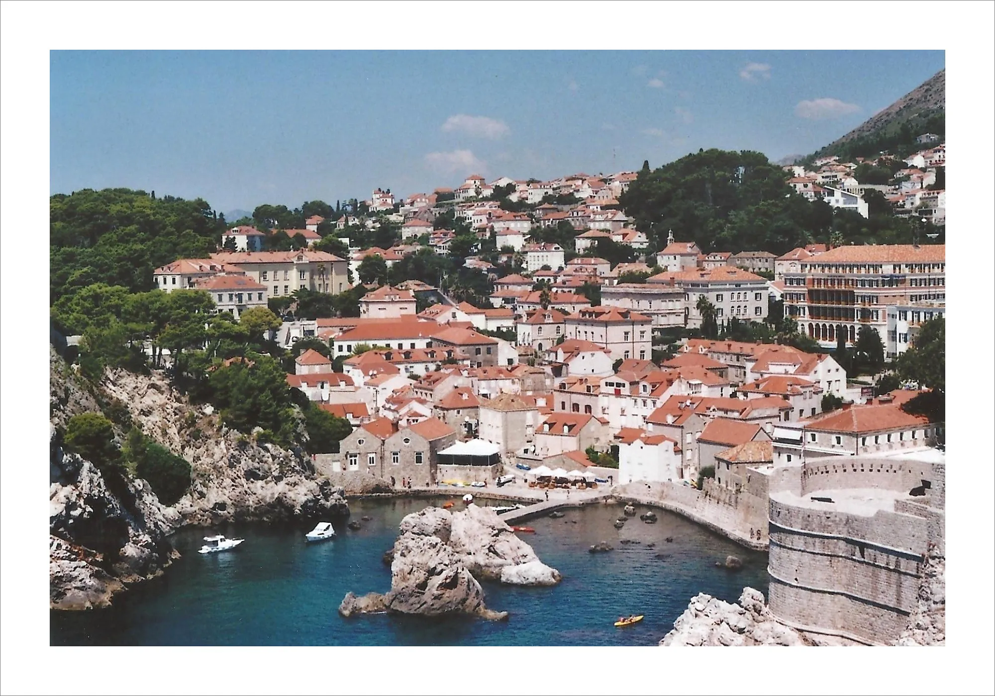 Dubrovnik fortress walls and turquoise harbor with boats on film.