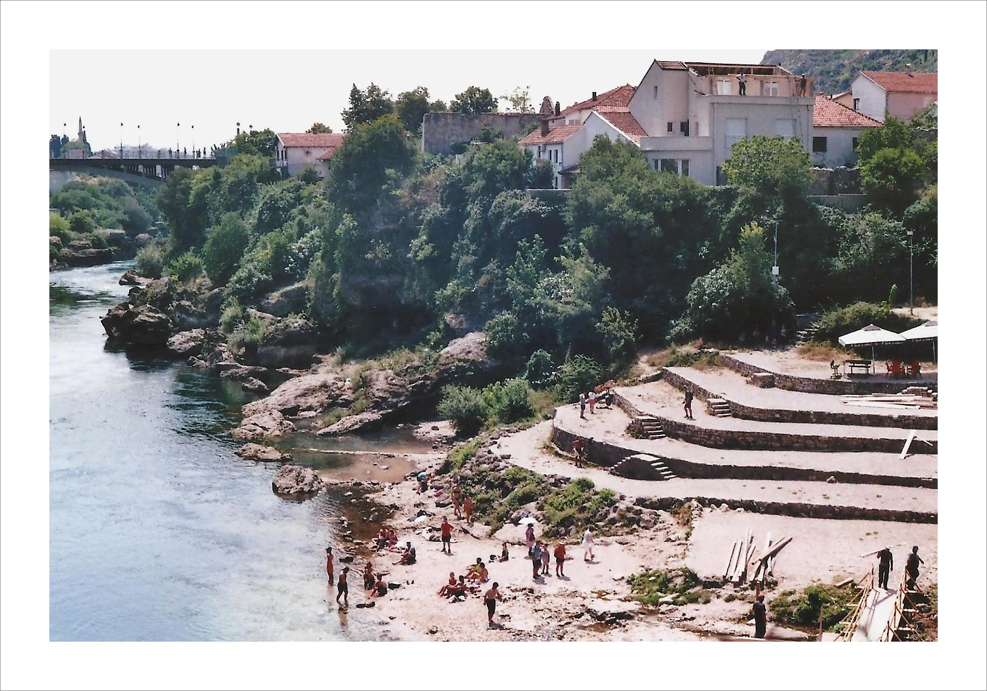 Small beach in Mostar with people and buildings.