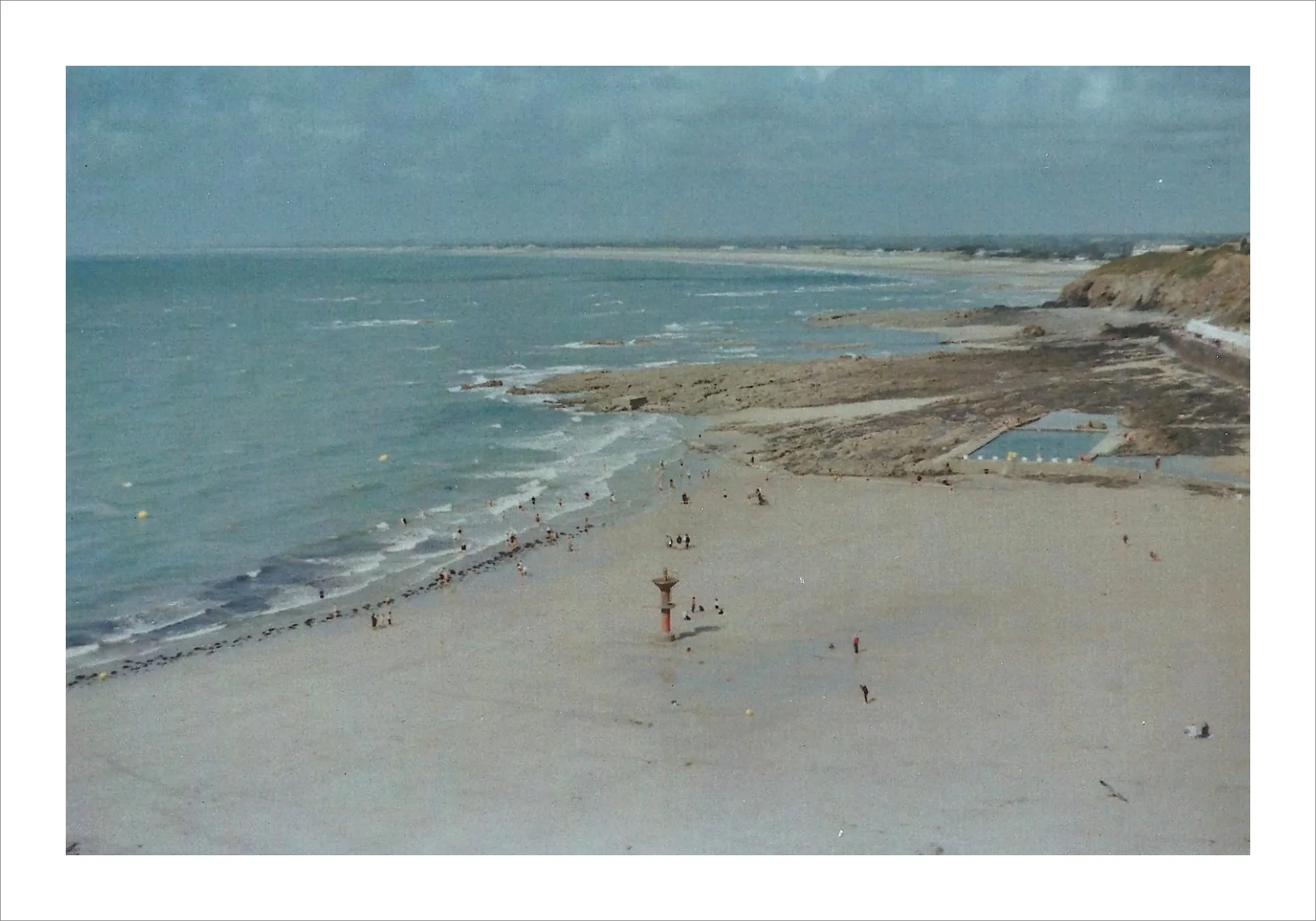 Beach with breakwater and distant shoreline on overcast day.