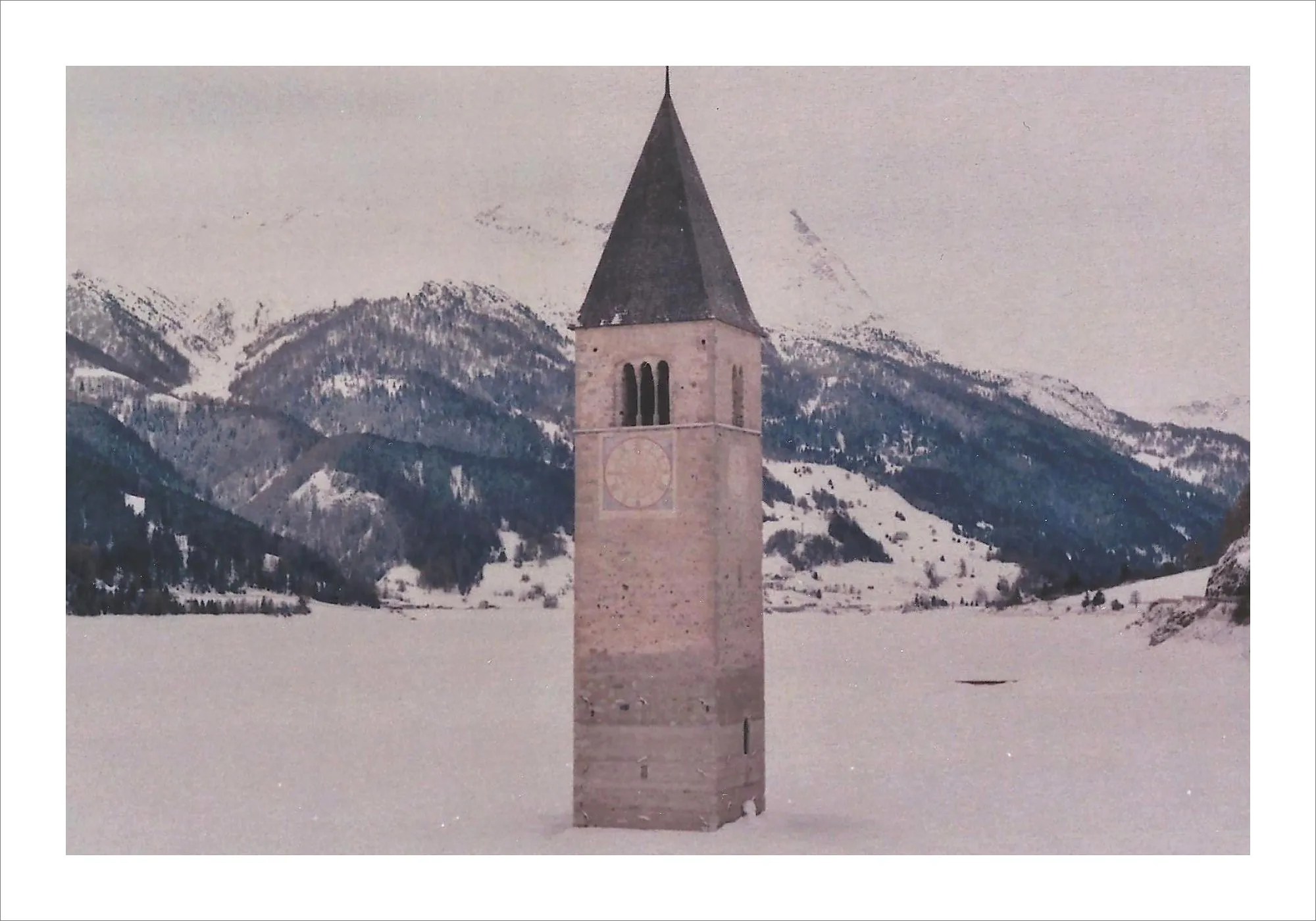 Church bell tower emerging from frozen Alpine lake in winter.