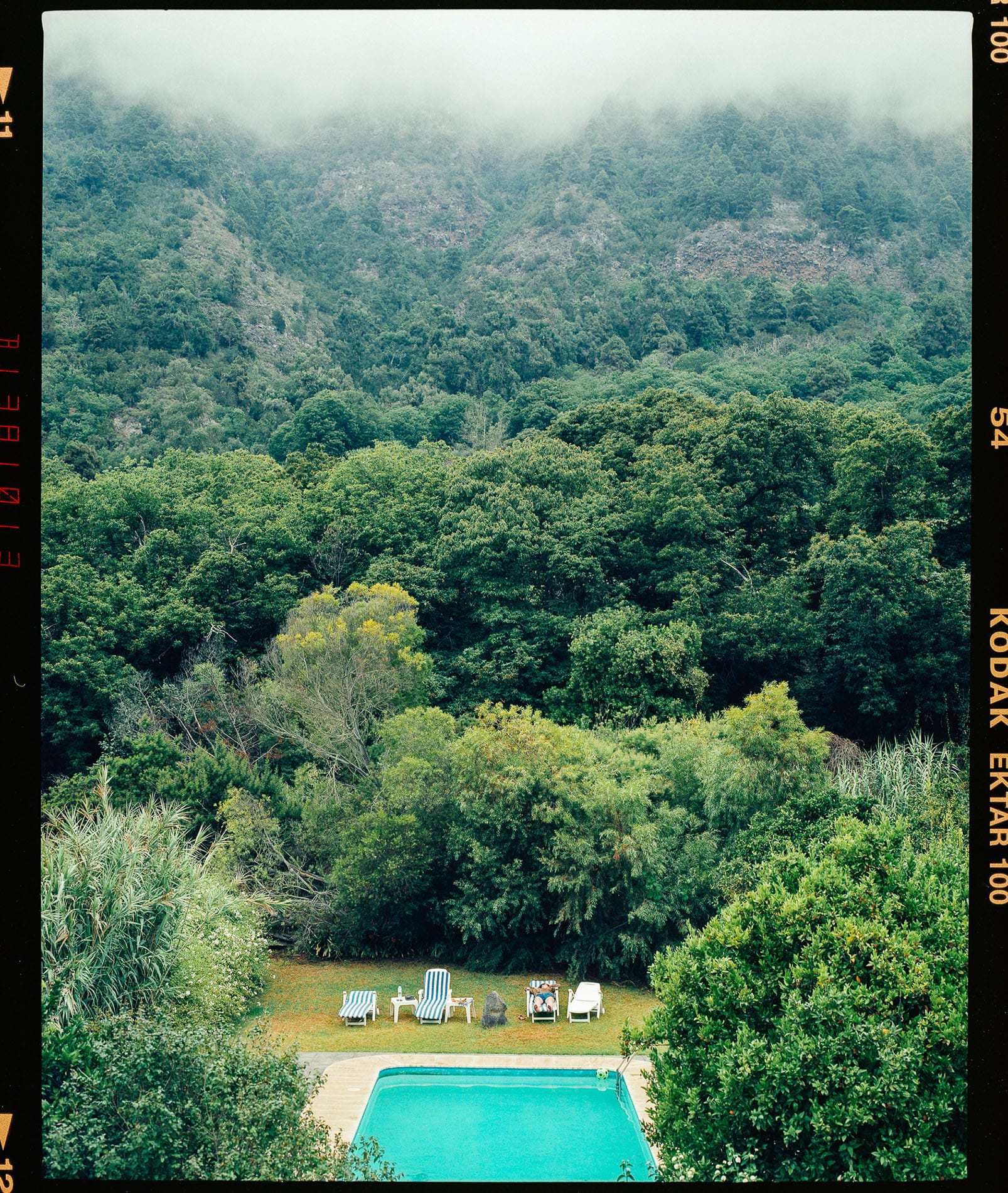 Swimming pool with lounge chairs and misty hills in background on Ektar 100 film.
