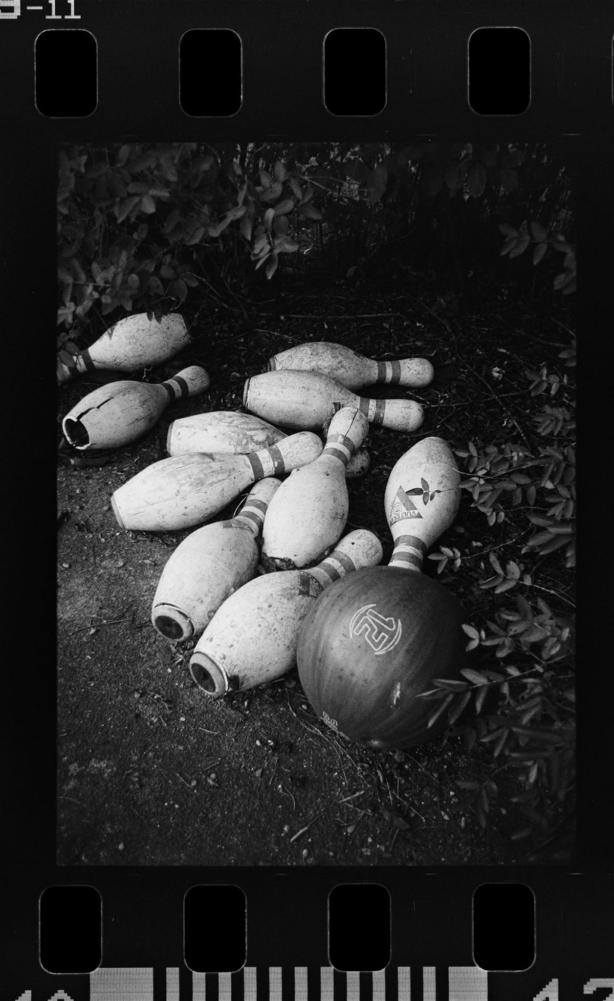 Vintage bowling pins scattered on pavement shot on black and white film.