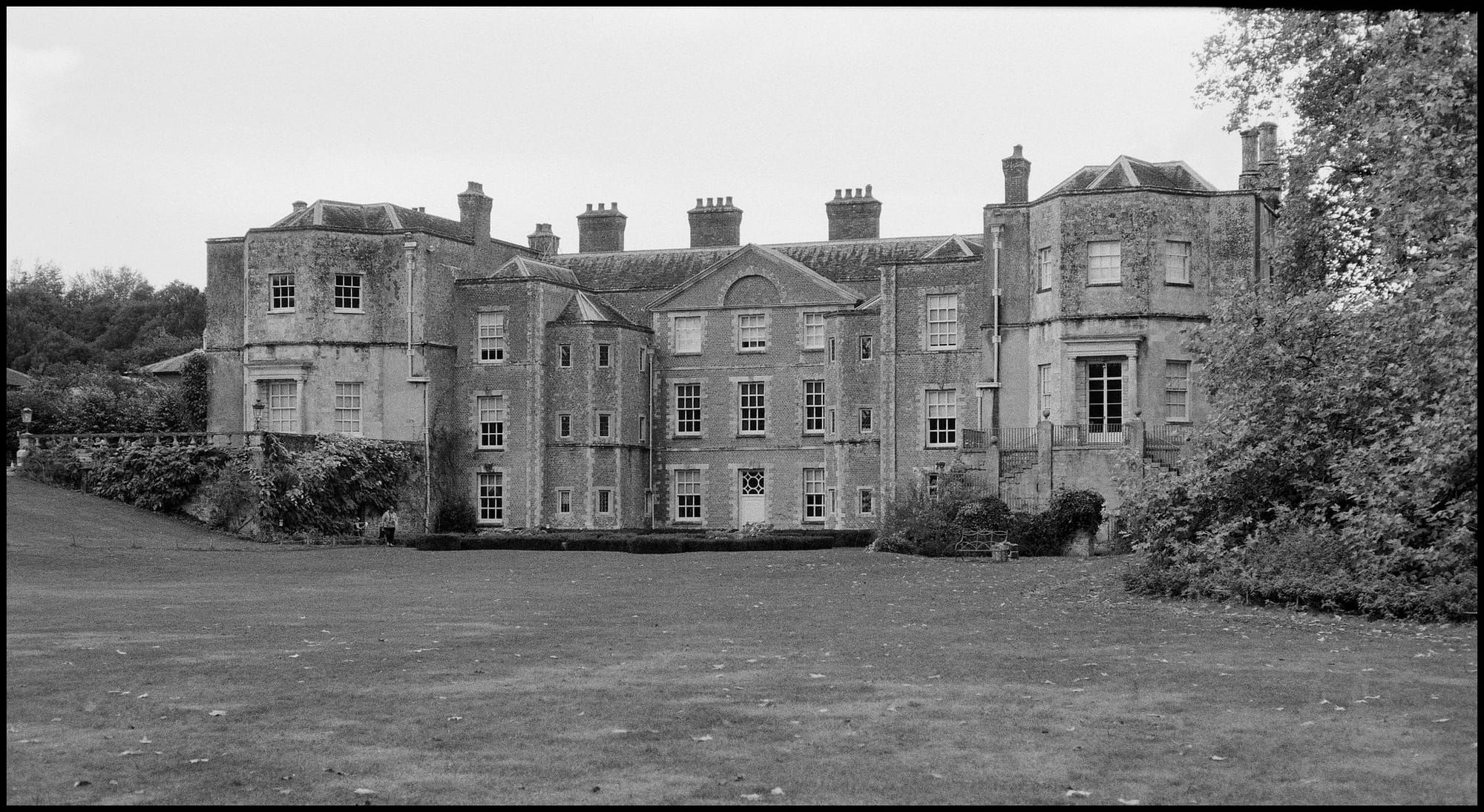 Black and white photo of weathered British manor house with chimneys.