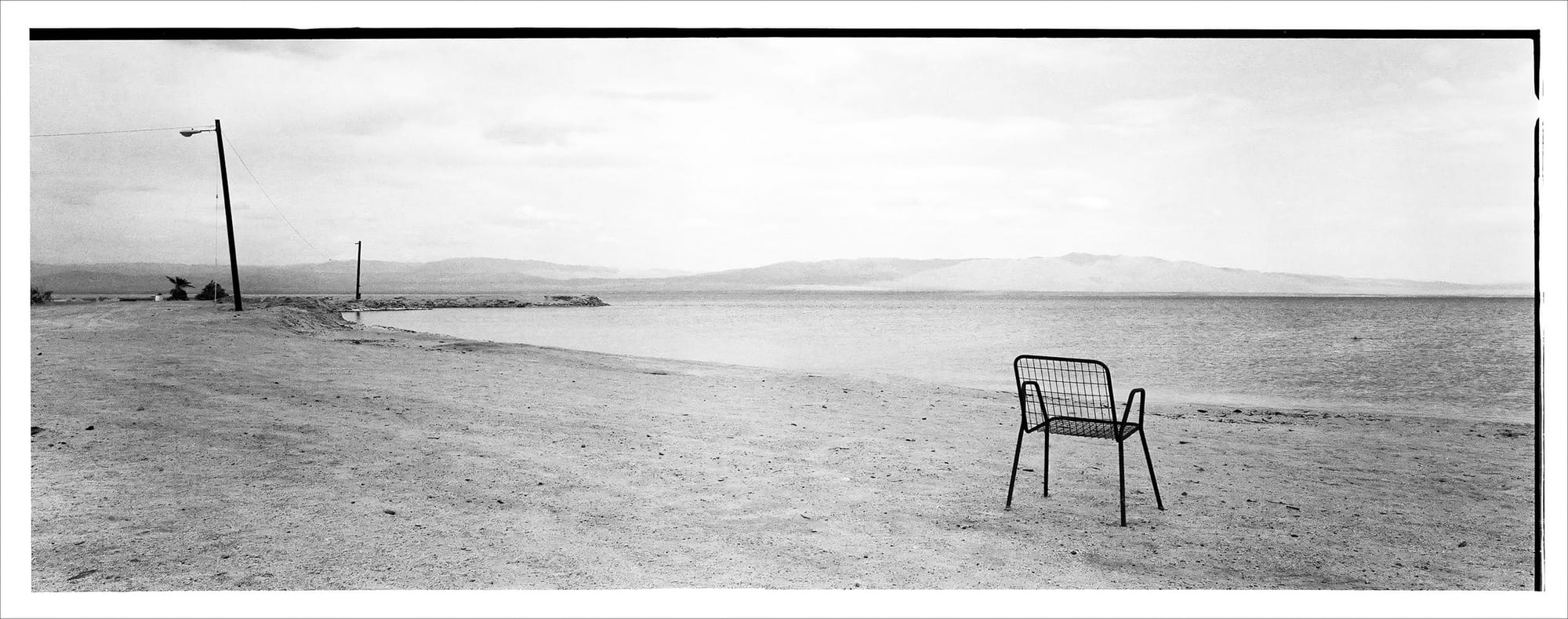 Black and white picture of a lone chair on a quiet beach with a vast, empty horizon.