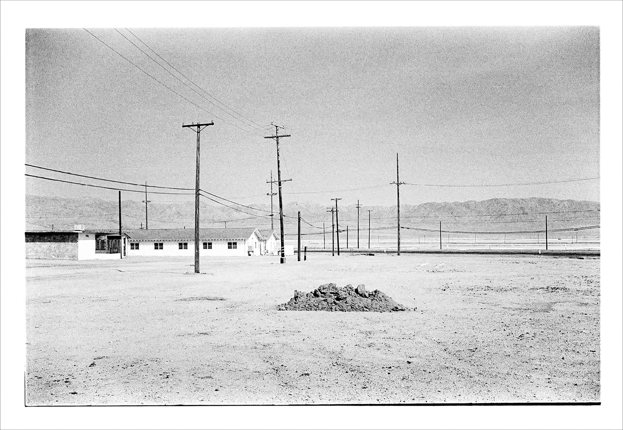 Black and white photo of rural landscape with power lines and buildings.