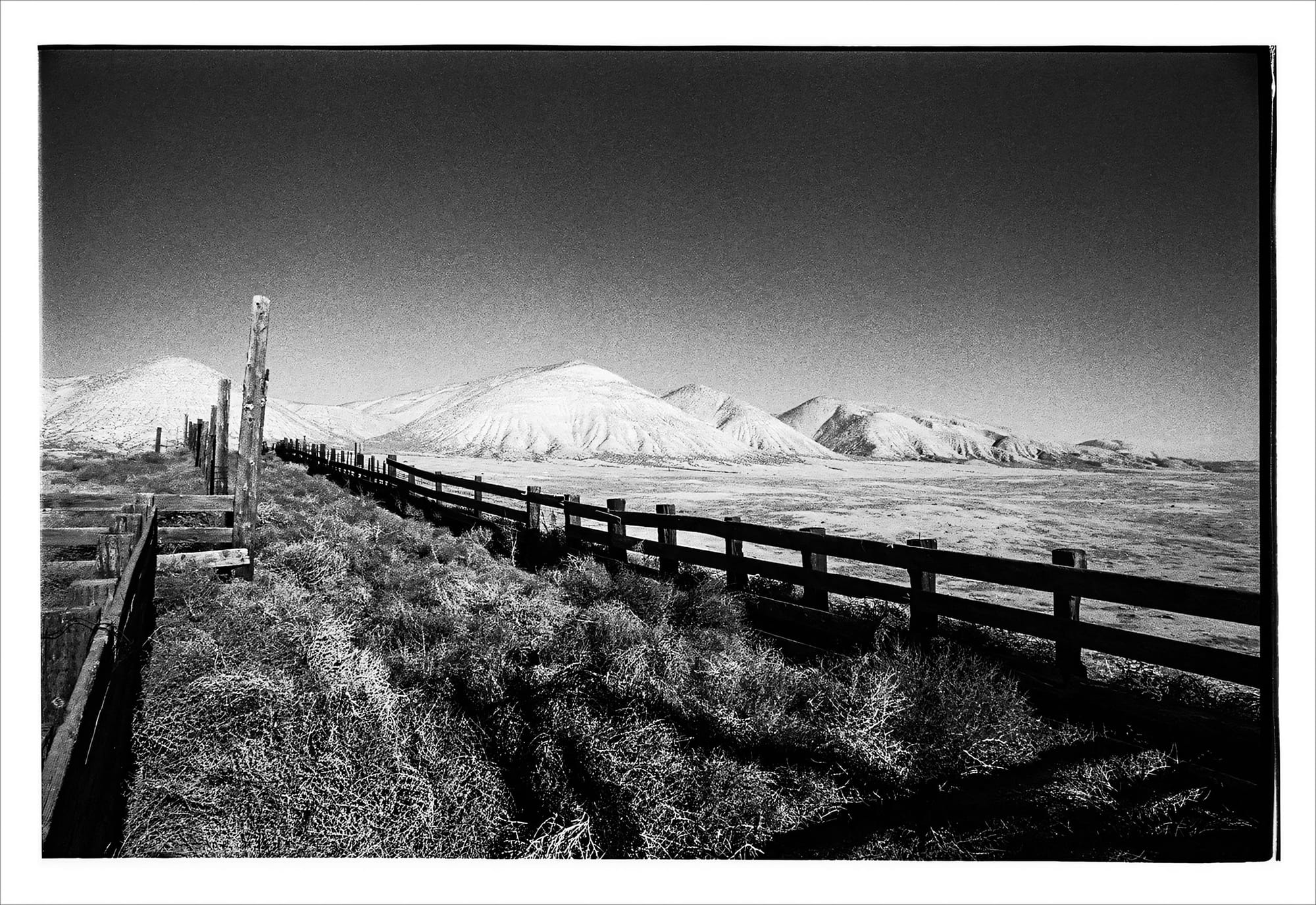 Black and white photo of a rural landscape with a fence in the foreground.