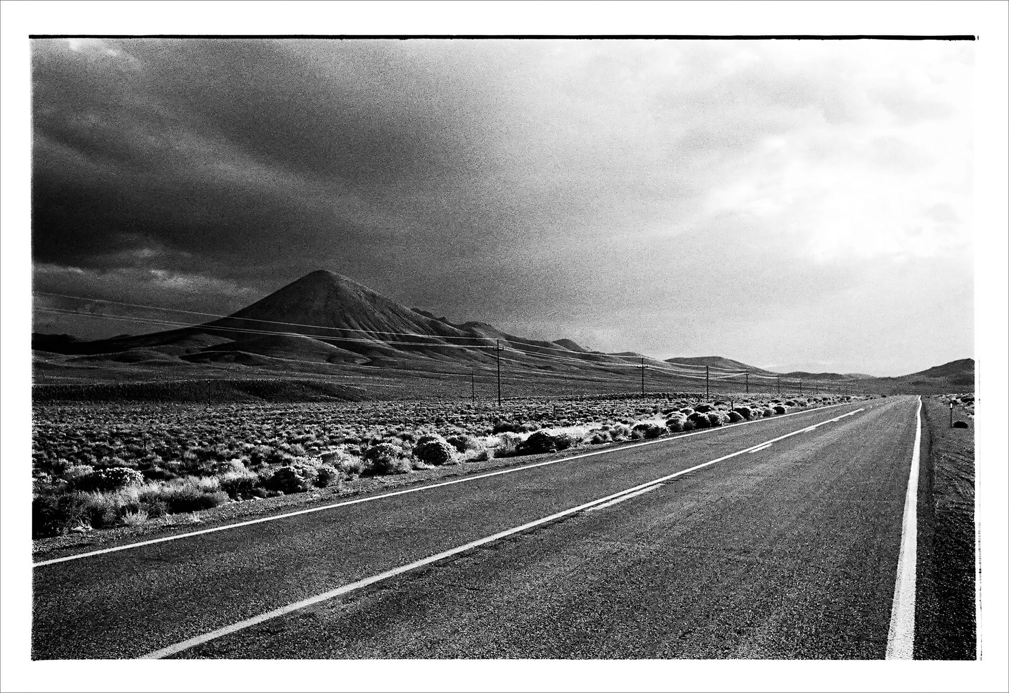 Black and white photo of a long, empty road leading to a distant mountain.